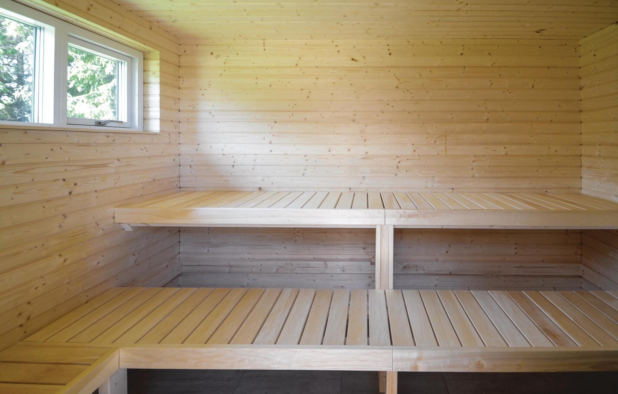 Interior de una cabaña de madera con dos niveles de espacios de asiento, un ventanal en el nivel superior y vista a árboles fuera.