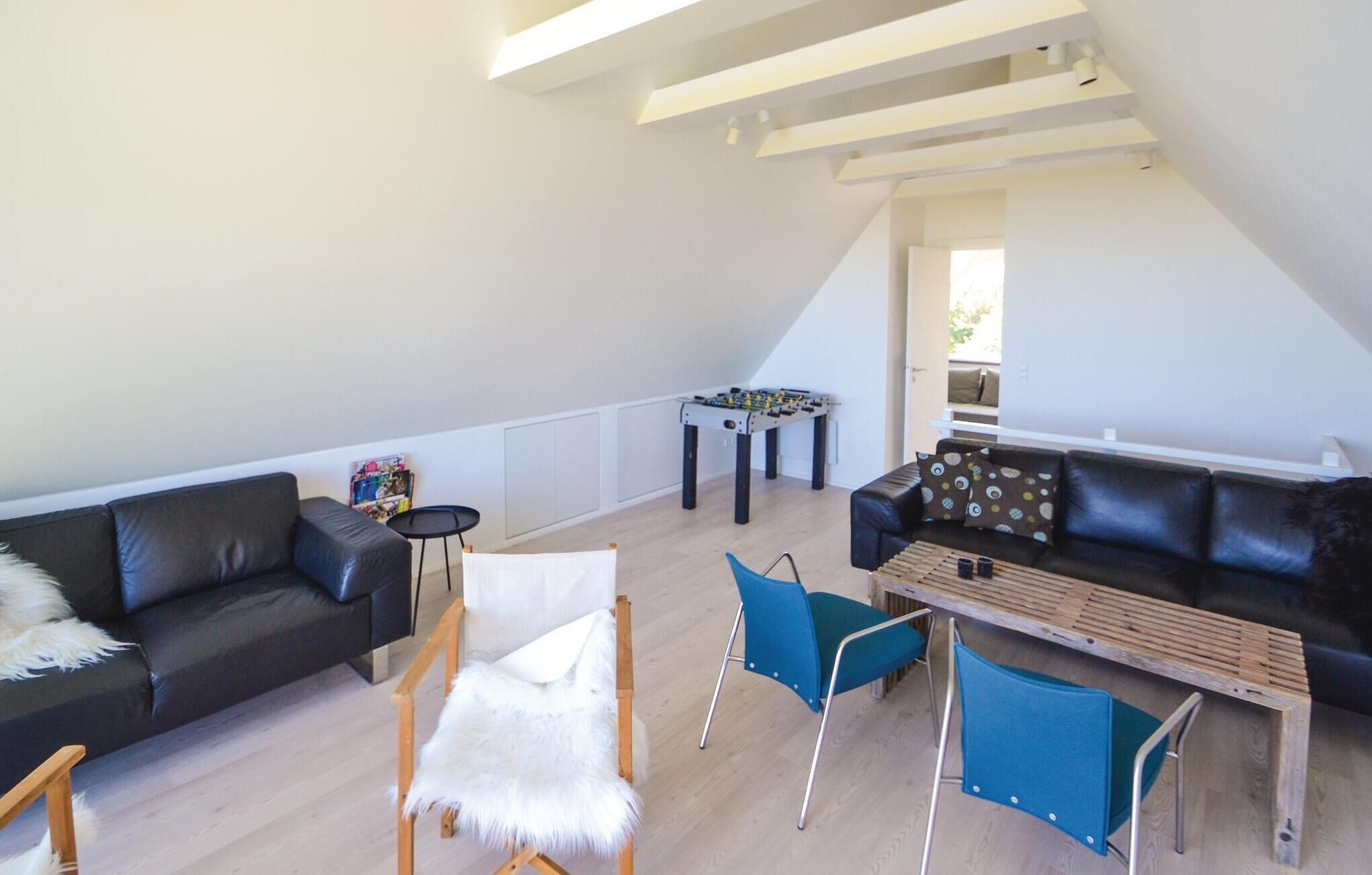 Un loft spacieux avec un plafond haut, un canapé en cuir noir, une table basse en bois et une chaise bleue.