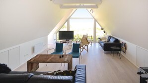 A modern loft-style living room with a sloped ceiling, a large TV, a wooden coffee table, a sofa, and a chair. - 6 bedroom stunning home in Grenaa (Grenaa)