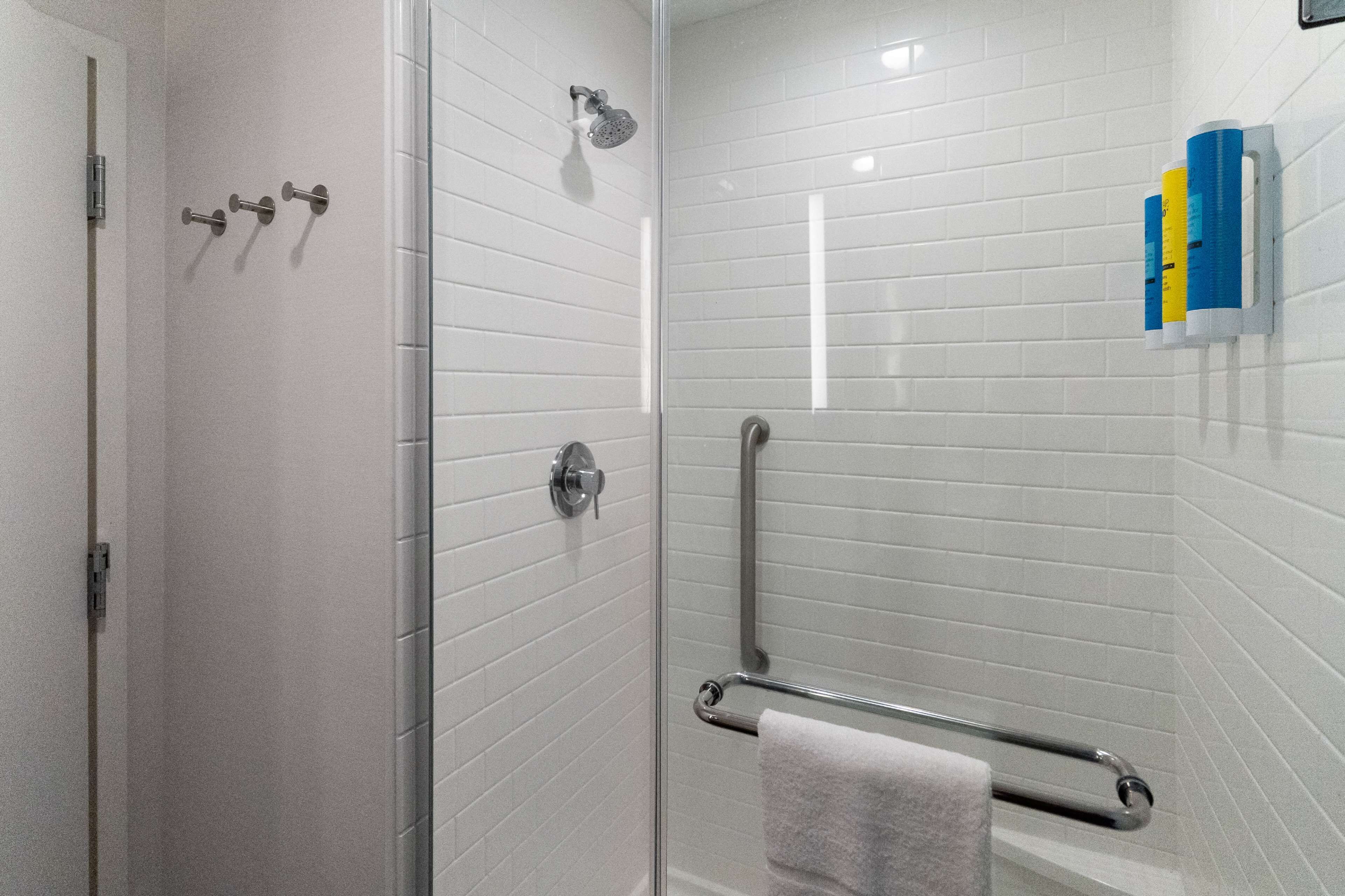 A modern bathroom with a glass shower enclosure, white tiled walls, and a handrail.