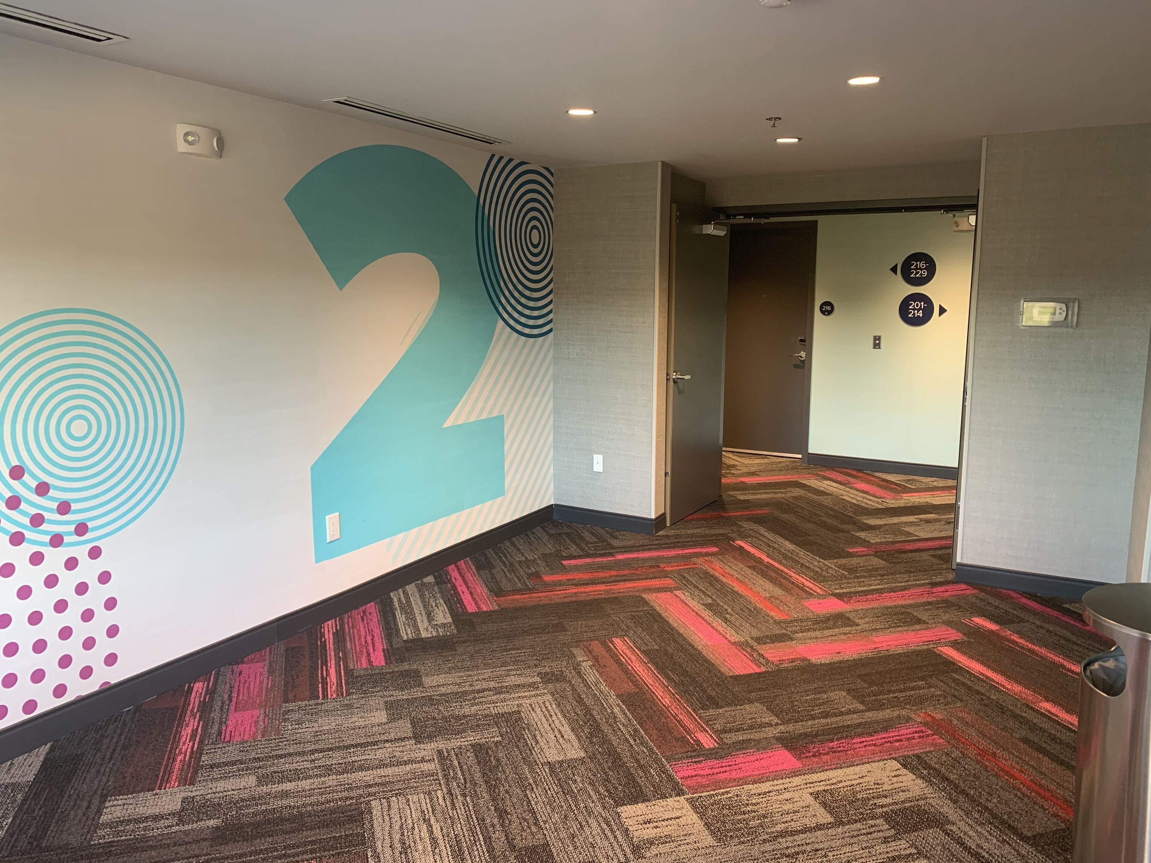 A hallway with a large number '2' on the wall, carpeted with a geometric pattern, and doors labeled with room numbers.