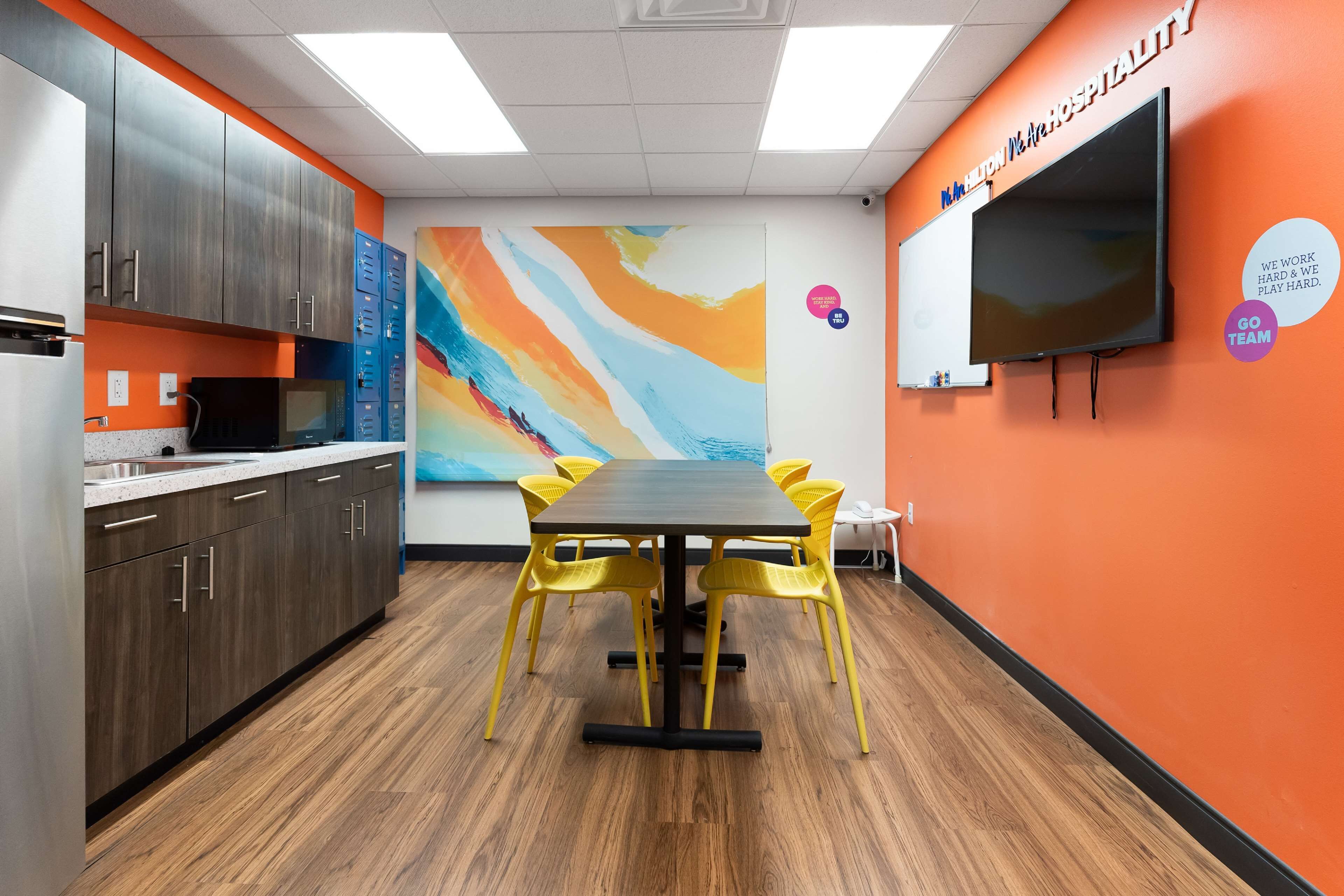 A conference room with a large table, yellow chairs, a TV, and a colorful abstract painting on the wall.