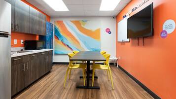 A conference room with a large table, yellow chairs, a TV, and a colorful abstract painting on the wall.