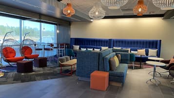 A modern lounge area with seating arrangements, including a blue sofa and red chairs, and a large window providing a view outside.