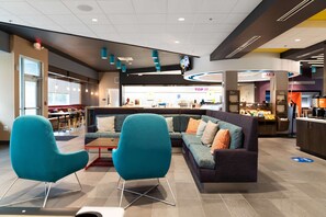 Eine moderne Lobby mit einer Eckcouch, Türkis-farbenen Sesseln, einer Kaffeebar und einem sichtbaren Restaurantbereich.