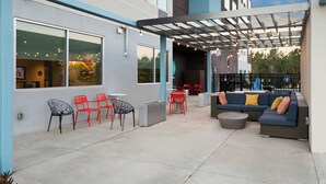 Un patio al aire libre con sillas rojas, un sofá azul con cojines y una pérgola con luces colgantes.