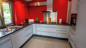 A modern kitchen with white cabinets, a stainless steel range hood, and a red accent wall.