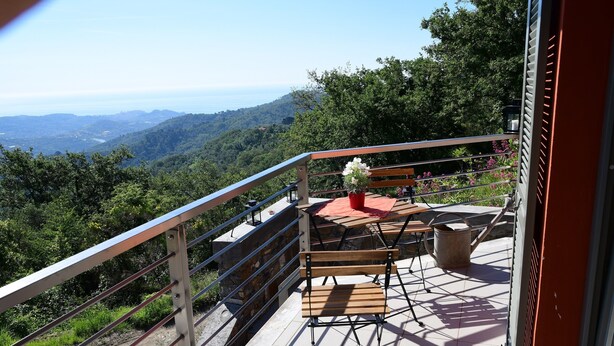 A balcony with a view of a mountainous landscape, a wooden bench, and a table with a red umbrella.