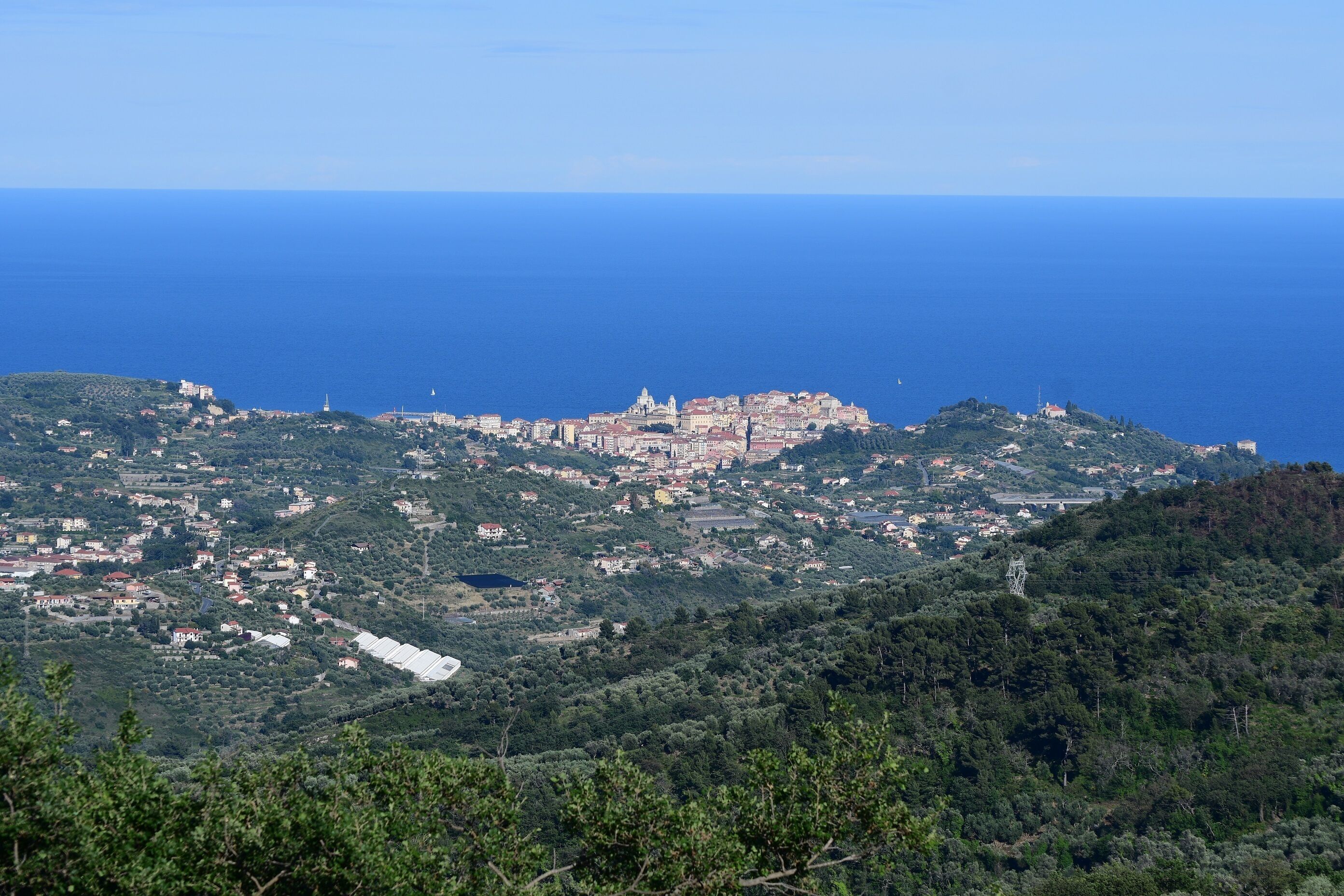 Uma vila costeira com uma igreja imponente no alto de uma colina, cercada por vegetação exuberante e vista clara do mar.