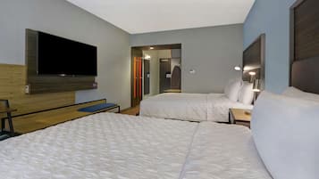 Una habitación de hotel con dos camas, un televisor montado en la pared y un escritorio pequeño.