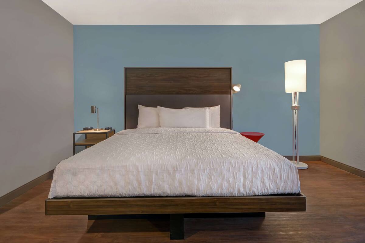Een moderne slaapkamer met een houten bed, een nachtkastje, een rode bijzettafel en een vloerlamp.