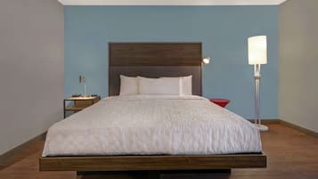 A modern bedroom with a wooden bed frame, a nightstand, a red side table, and a floor lamp.