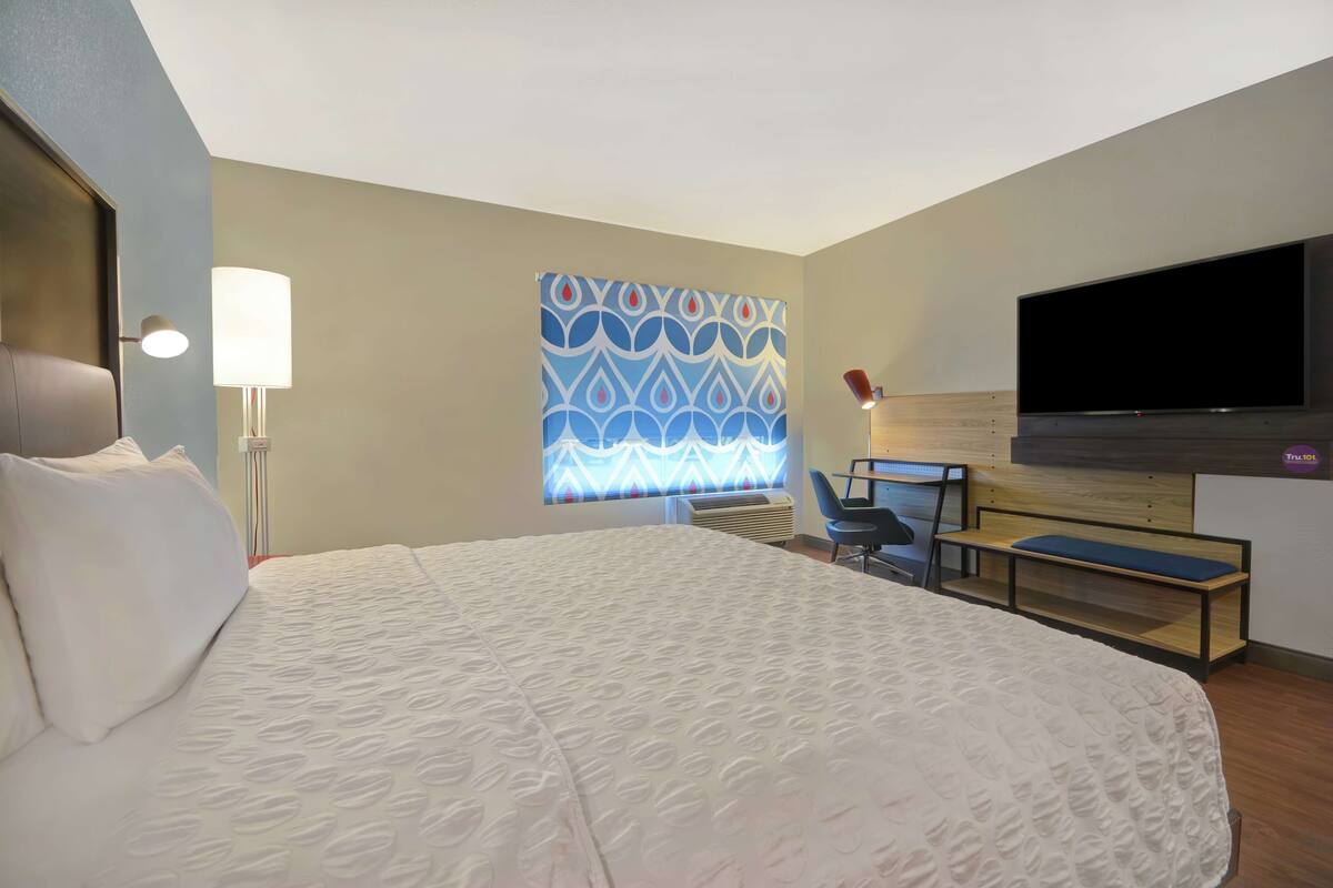 Een hotelkamer met een groot bed, een bureau met stoel, een flatscreen televisie en een behangen wand.