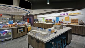 Un espace moderne dédié au petit-déjeuner, avec un comptoir où sont exposés divers aliments et un panneau indiquant : « TOP IT BREAKFAST ».