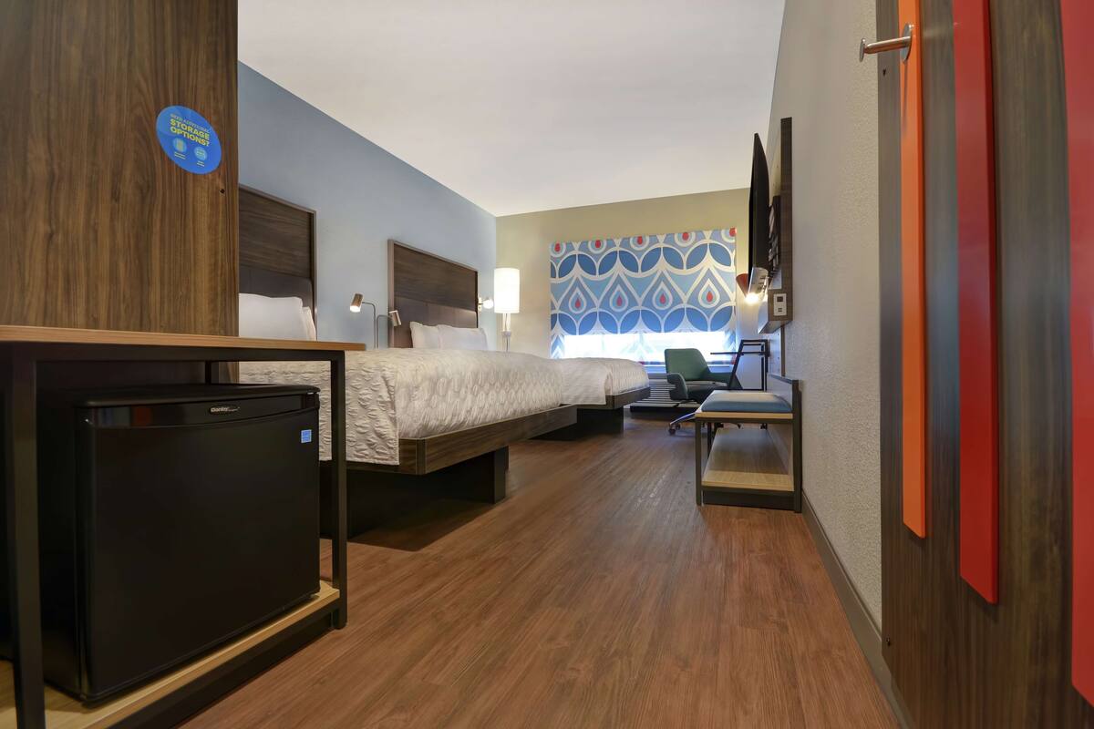 Een hotelkamer met een bed, een bureau, een stoel, een kleine koelkast en een televisie aan de muur.