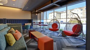 Un espace de détente moderne comprenant un canapé, un pouf, des fauteuils suspendus et une table en bois.