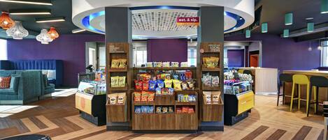A snack kiosk with a variety of packaged goods, a seating area with a blue sofa, and a counter with a cash register.