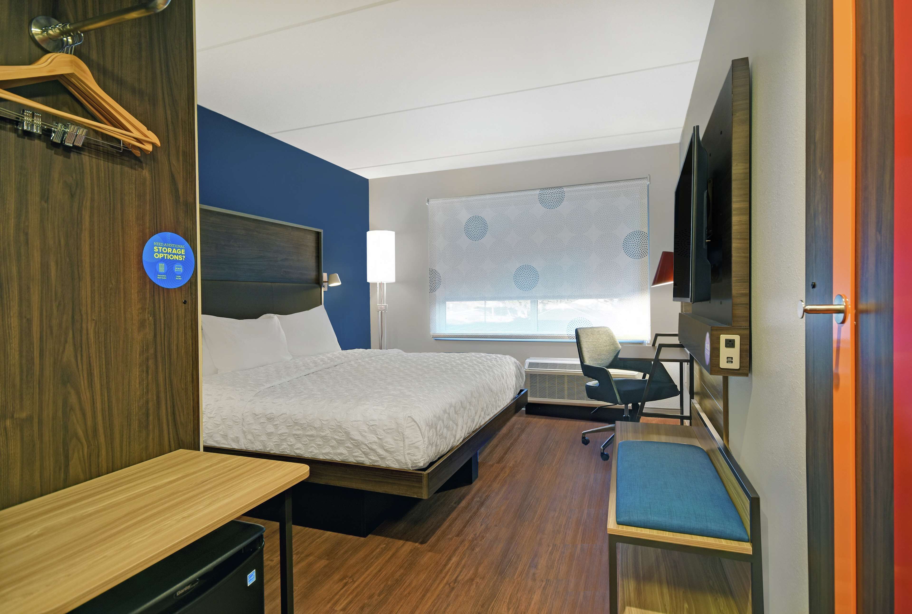 A hotel room with a bed, desk, chair, and a TV.