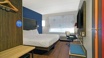 A hotel room with a bed, desk, chair, and a TV.