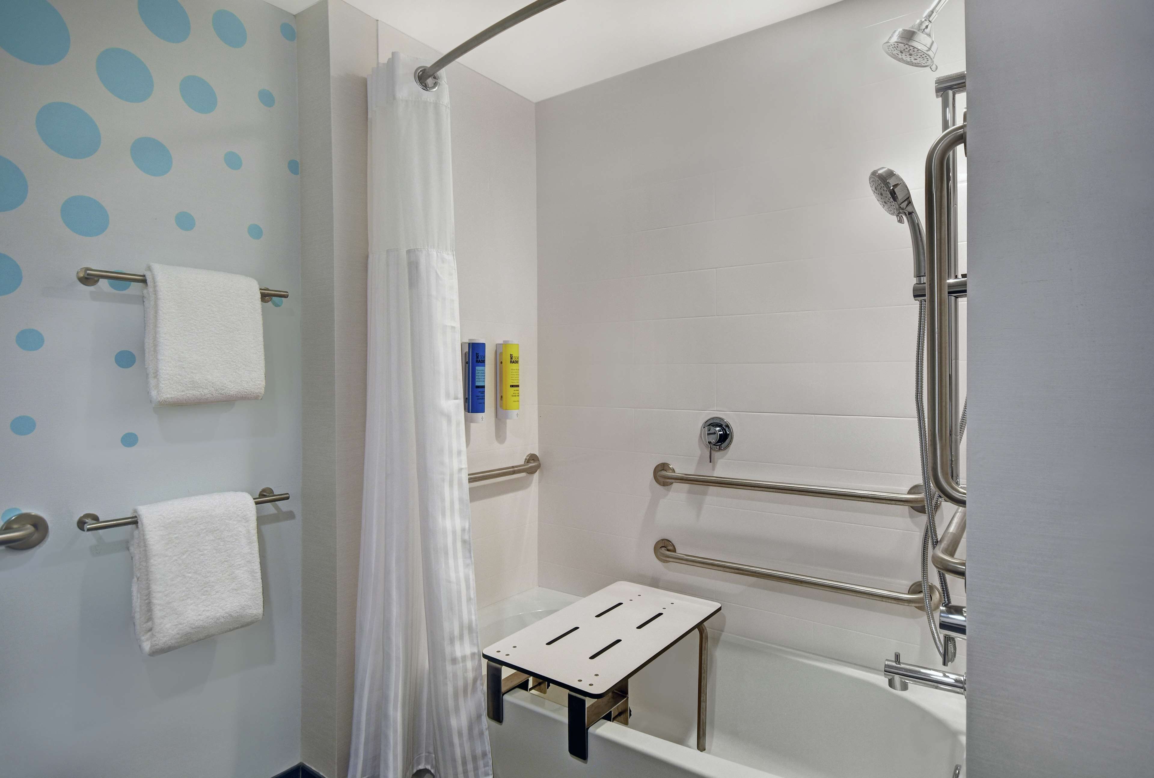 Ein modernes Badezimmer mit Dusche, Haltegriffen, einer weißen Badewanne und einem Handtuchhalter.