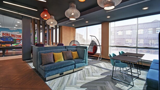 A modern lounge area with a blue sofa, a hanging chair, and a table with chairs. - Tru By Hilton Burlington (Burlington)