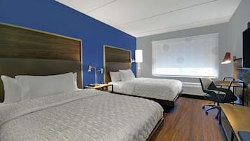 Habitación de hotel con dos camas, un escritorio, una silla y una ventana con vistas.