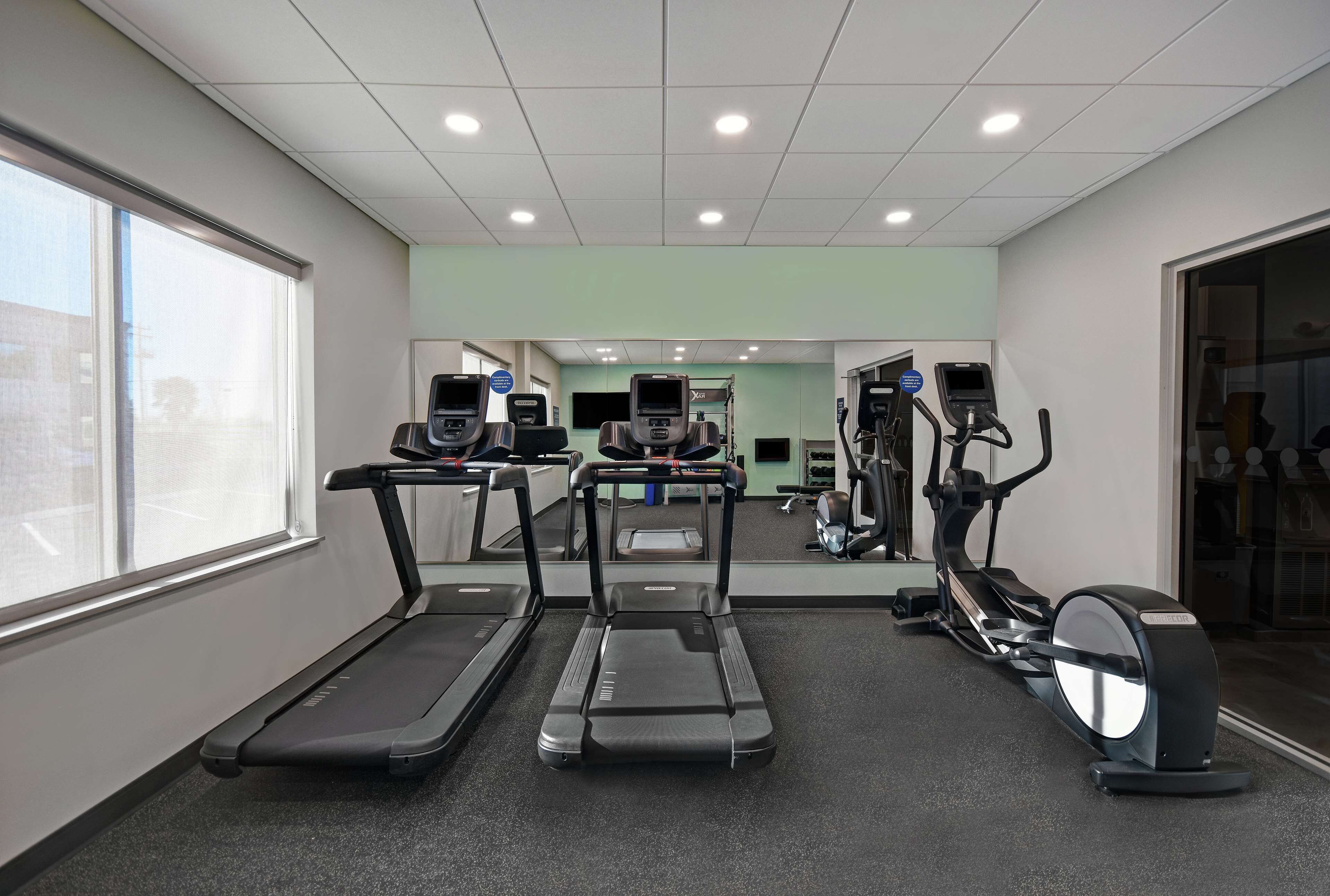 A gym with treadmills, elliptical machines, and a mirrored wall.