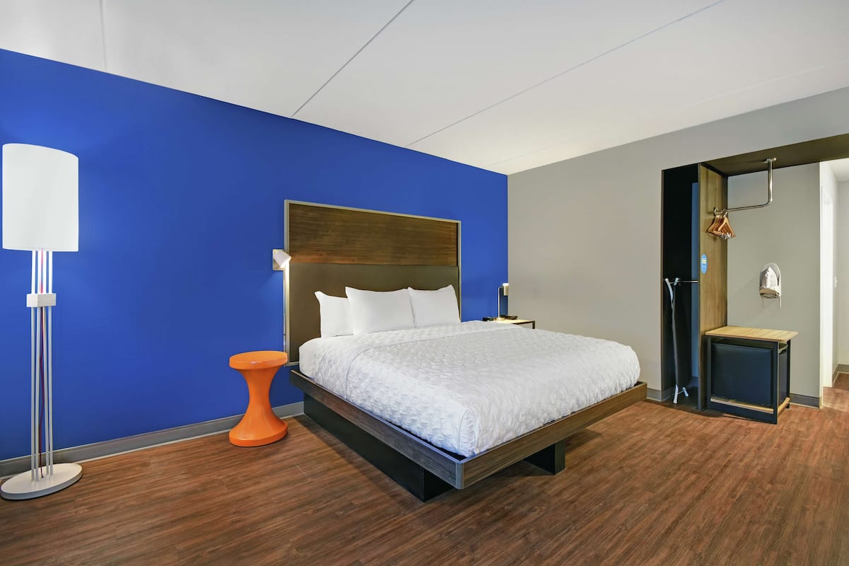 A modern hotel room with a large bed, a nightstand, a floor lamp, and a wooden bench.