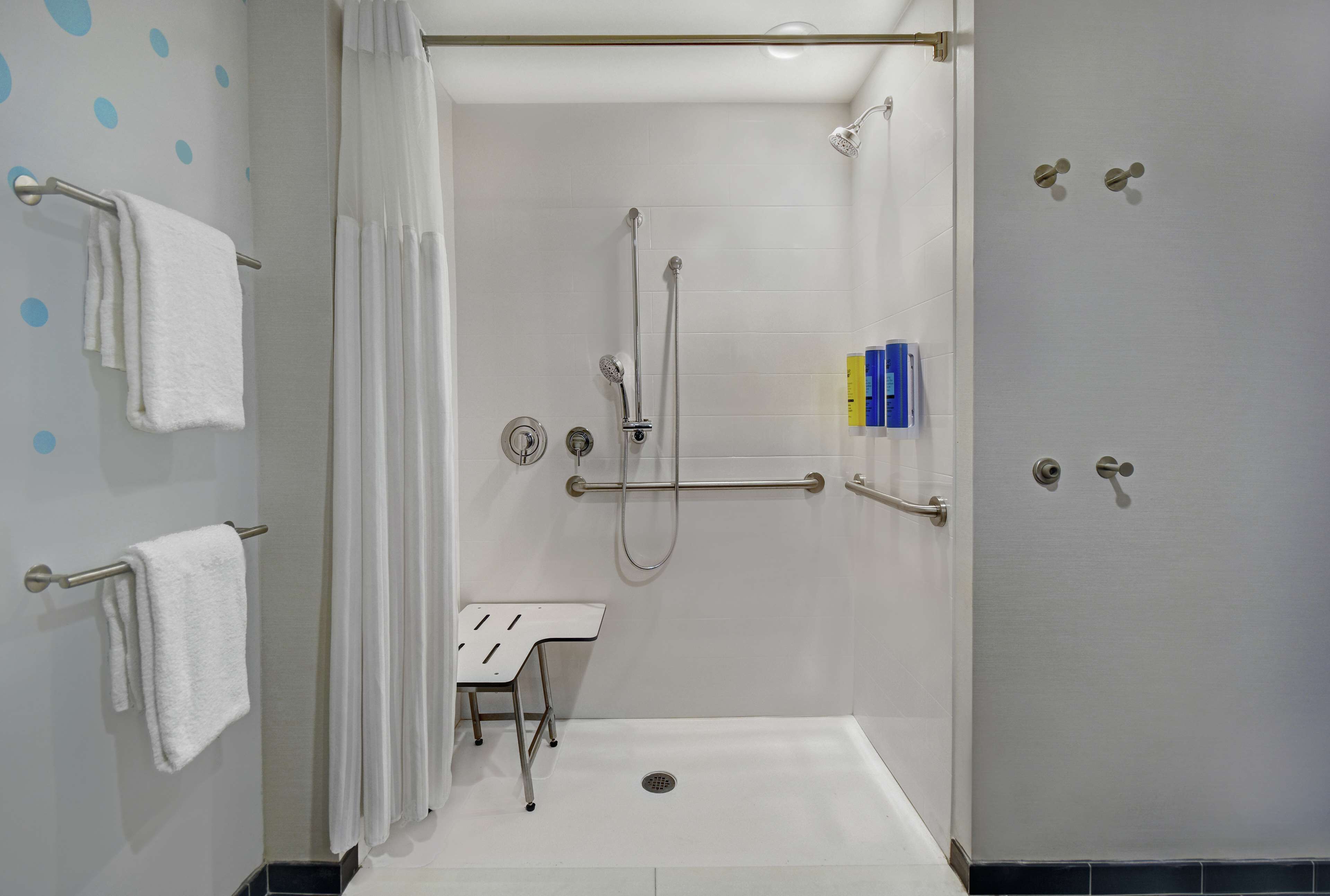 Un baño moderno con cabina de ducha, barras de apoyo, un lavabo blanco y un perchero para toallas.