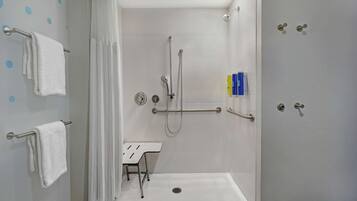 Un baño moderno con cabina de ducha, barras de apoyo, un lavabo blanco y un perchero para toallas.