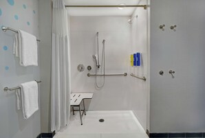 Un baño moderno con cabina de ducha, barras de apoyo, un lavabo blanco y un perchero para toallas.