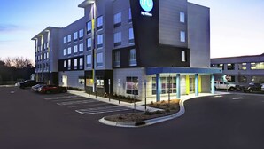 A modern hotel with a prominent 'TRU by Hilton' sign, a parking lot, and a clear sky. - Tru By Hilton Burlington (Burlington)