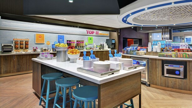A modern breakfast area with a central island, bar stools, and a variety of food items and beverages.