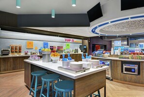 A modern breakfast area with a central island, bar stools, and a variety of food items and beverages.