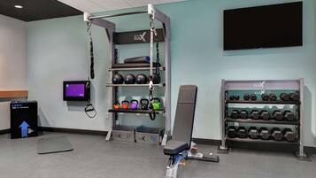 A gym with a pull-up bar, kettlebells, dumbbells, and a TV screen.