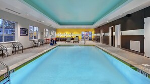 An indoor swimming pool with clear water, surrounded by chairs and tables, and a sign indicating no lifeguard on duty.