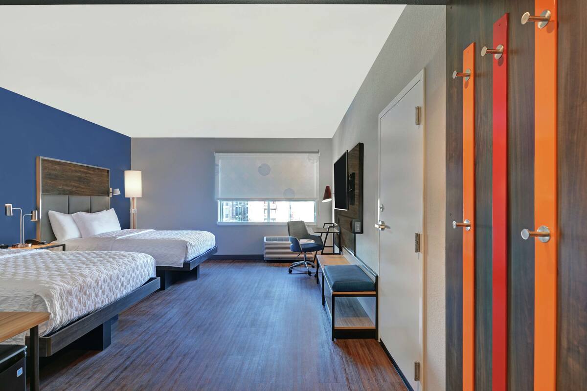 Une chambre d’hôtel avec deux lits, un bureau, une chaise, une télévision et une fenêtre.