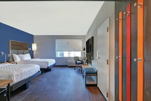 A hotel room with two beds, a desk, a chair, a TV, and a window.
