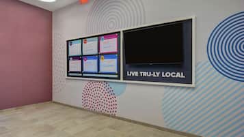 A room with a bulletin board displaying various notices, a large window with a 'LIVE TRU-LY LOCAL' sign, and a patterned wall design.