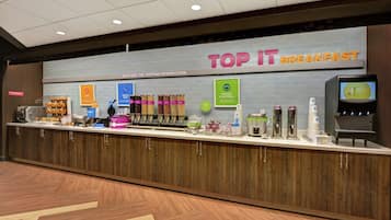 Un espace réservé au petit-déjeuner, avec une pancarte indiquant « TOP IT BREAKFAST » et proposant divers plats et boissons.
