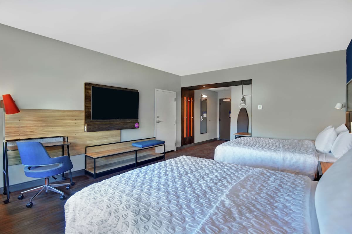 Une chambre d’hôtel avec deux lits, un bureau avec une chaise, un téléviseur fixé au mur et une porte donnant sur une autre pièce.