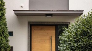 A modern building with a wooden door, a small window, and a stone pathway leading to the entrance.