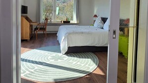 A bedroom with a bed, a desk, a chair, a TV, and a window with a view of trees.