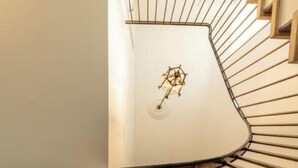 A spiral staircase with a geometric light fixture at the top, framed pictures on the walls, and a metal handrail.