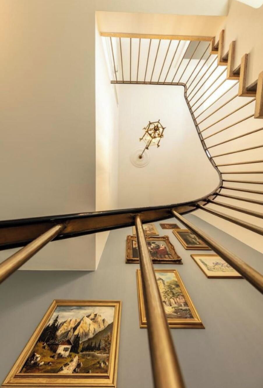 Eine Wendeltreppe mit einer Chandelüster, gerahmten Kunstwerken und Blick auf die obere Etage.