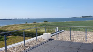 Une terrasse au bord de l’eau, dotée d’une rambarde en métal, d’un banc blanc et d’une allée pavée.
