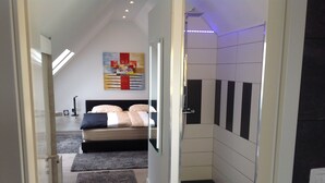 Une chambre moderne comprenant un lit, un espace douche et un couloir menant à une salle de bain.