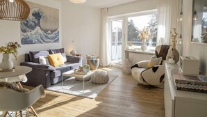 Una sala de estar moderna con un sofá, una mesa de centro y elementos decorativos. Hay un ventanal grande que proporciona luz natural y vistas al exterior.