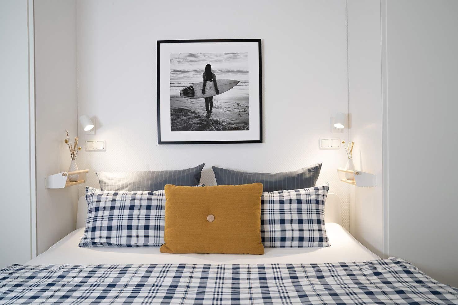 Ein Schlafzimmer mit einem Bett, einem gerahmten Bild von einem Surfer und Nachttischlampen.
