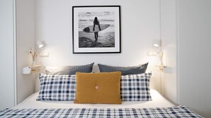 Un dormitorio con una cama, un cuadro enmarco de un surfista y lámparas de noche.